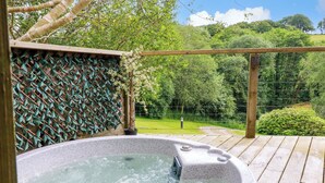Un jacuzzi en una terraza de madera con un muro de celosía y vistas a un jardín exuberante.