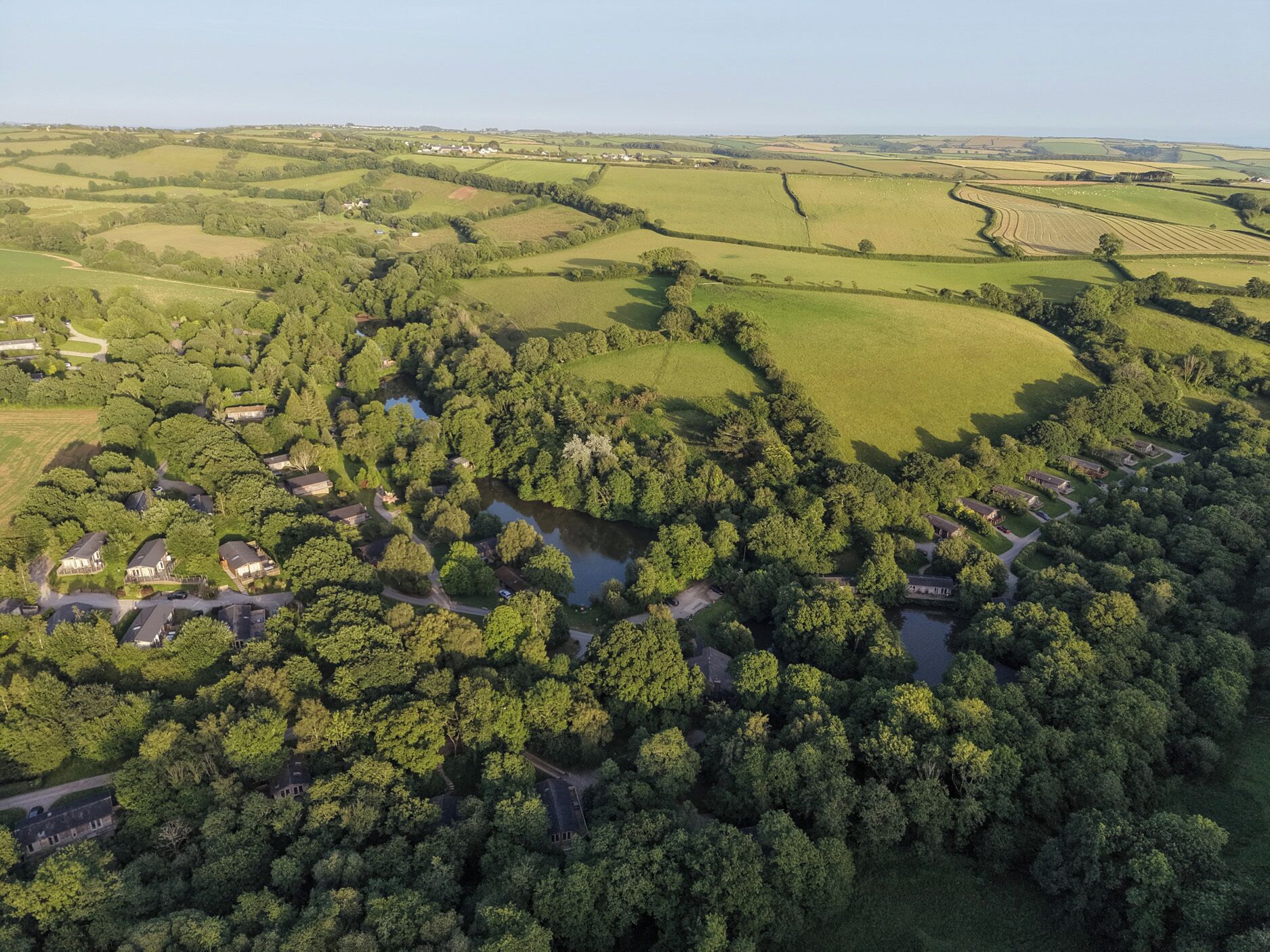 An aerial view of a rural area with scattered houses, a winding river, and rolling green fields.