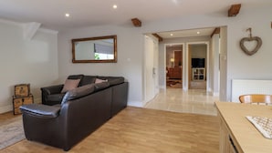 Un salon avec un canapé en cuir foncé, un parquet, un miroir et une décoration en forme de cœur accrochée au mur.