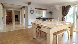 Un grand espace à manger avec une table et des bancs en bois, une cuisine à l’arrière-plan et une vue dégagée grâce à une grande fenêtre.