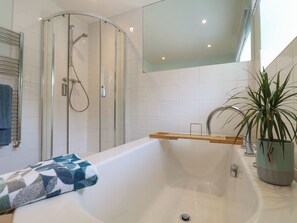 Un baño moderno con ducha de vidrio, bañera independiente y planta en maceta.
