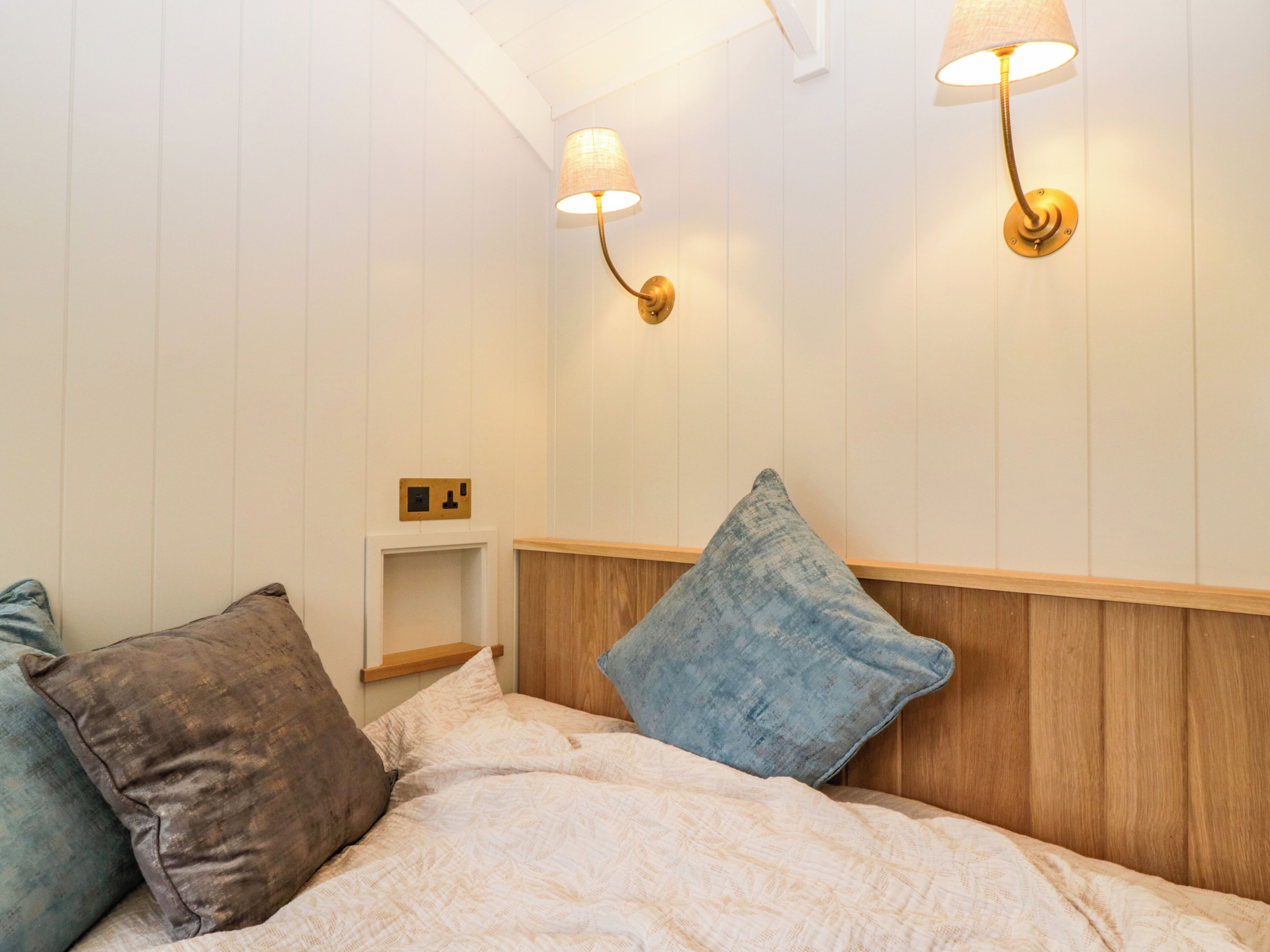 A neatly made bed with a headboard, two wall-mounted lamps, and a small bedside table with a power outlet.