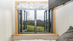 Een slaapkamer met een groot raam, een bed en uitzicht op een groen landschap.