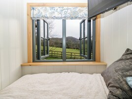 Un dormitorio con un ventanal grande, una cama y vistas a un paisaje verde.