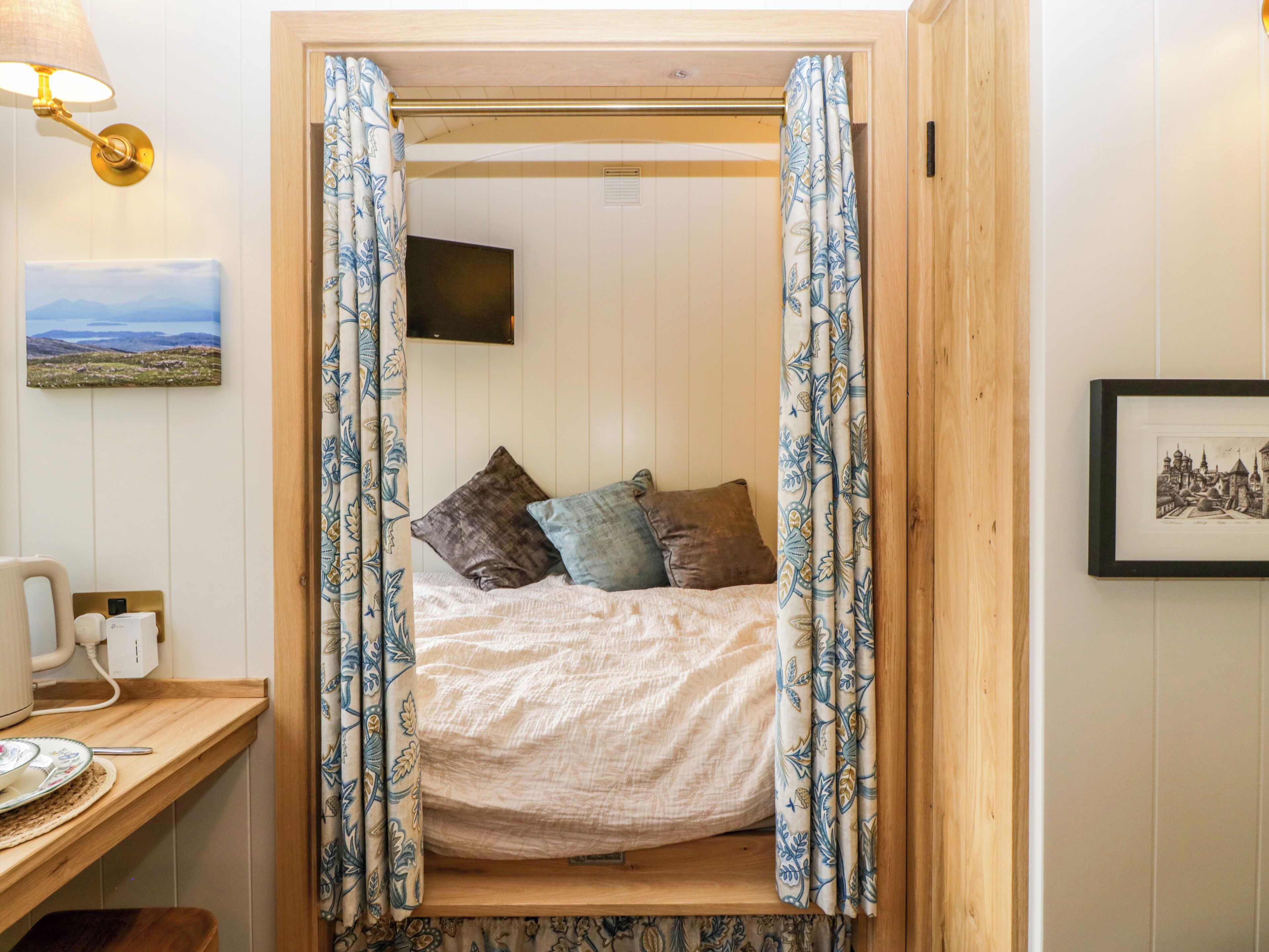 A cozy room with a bed, a desk with a lamp, and a painting on the wall.
