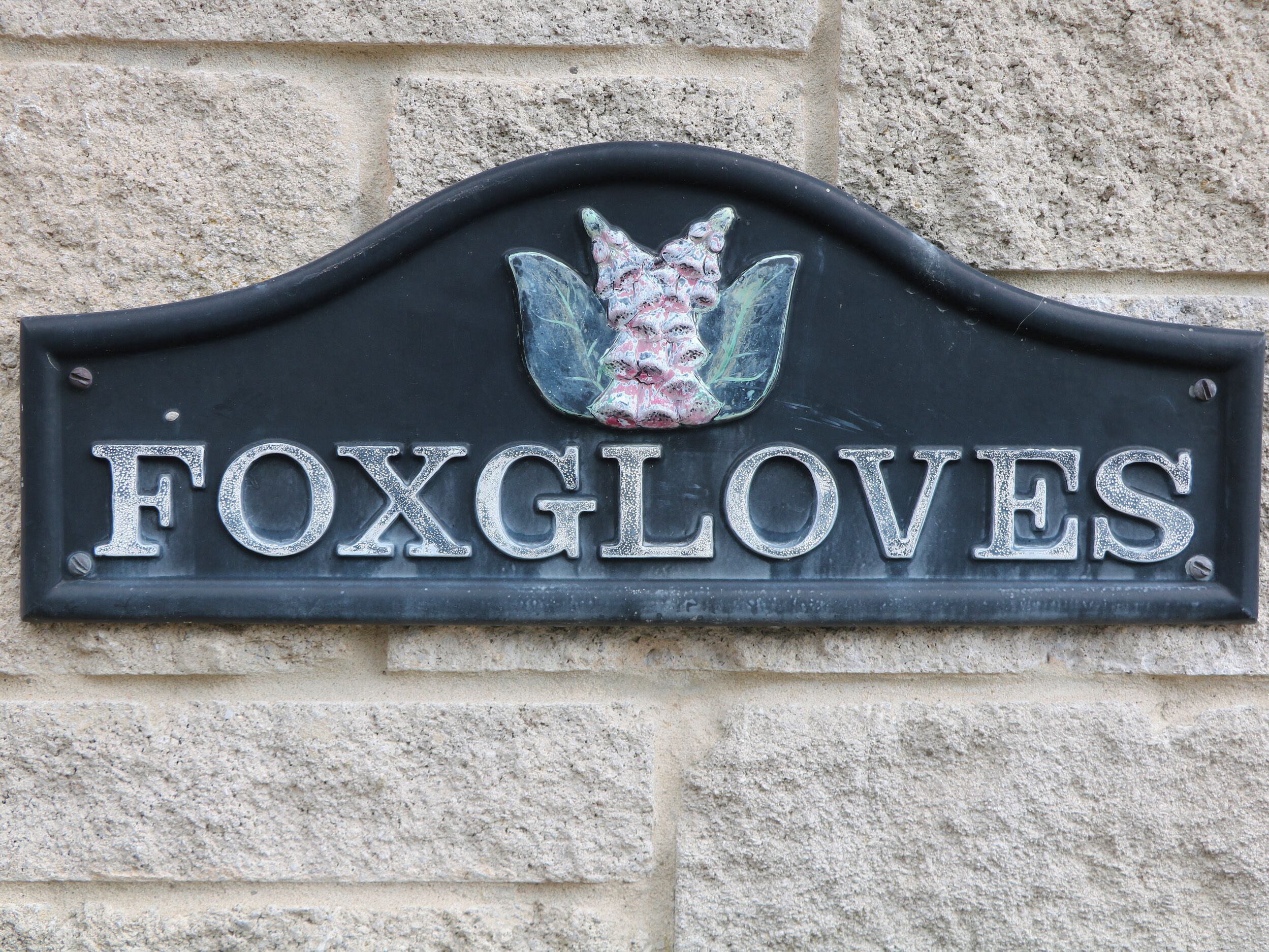 Un letrero de metal negro con la palabra "FOXGLOVES" y un emblema decorativo.