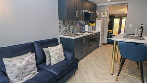 Une cuisine moderne avec des meubles sombres, un four à micro-ondes et un réfrigérateur. Le salon est doté d’un canapé bleu agrémenté de coussins décoratifs.