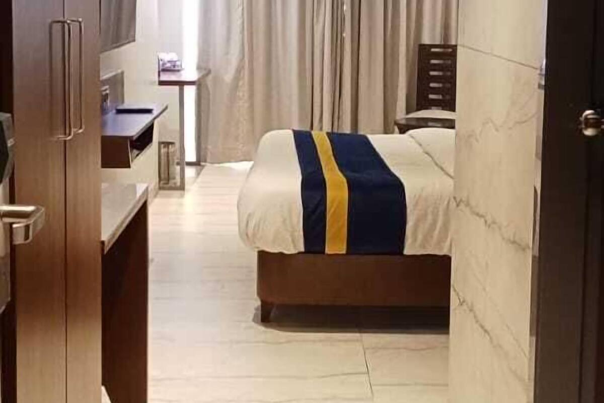 A hotel room with a bed, a desk, a television, and a window with curtains.