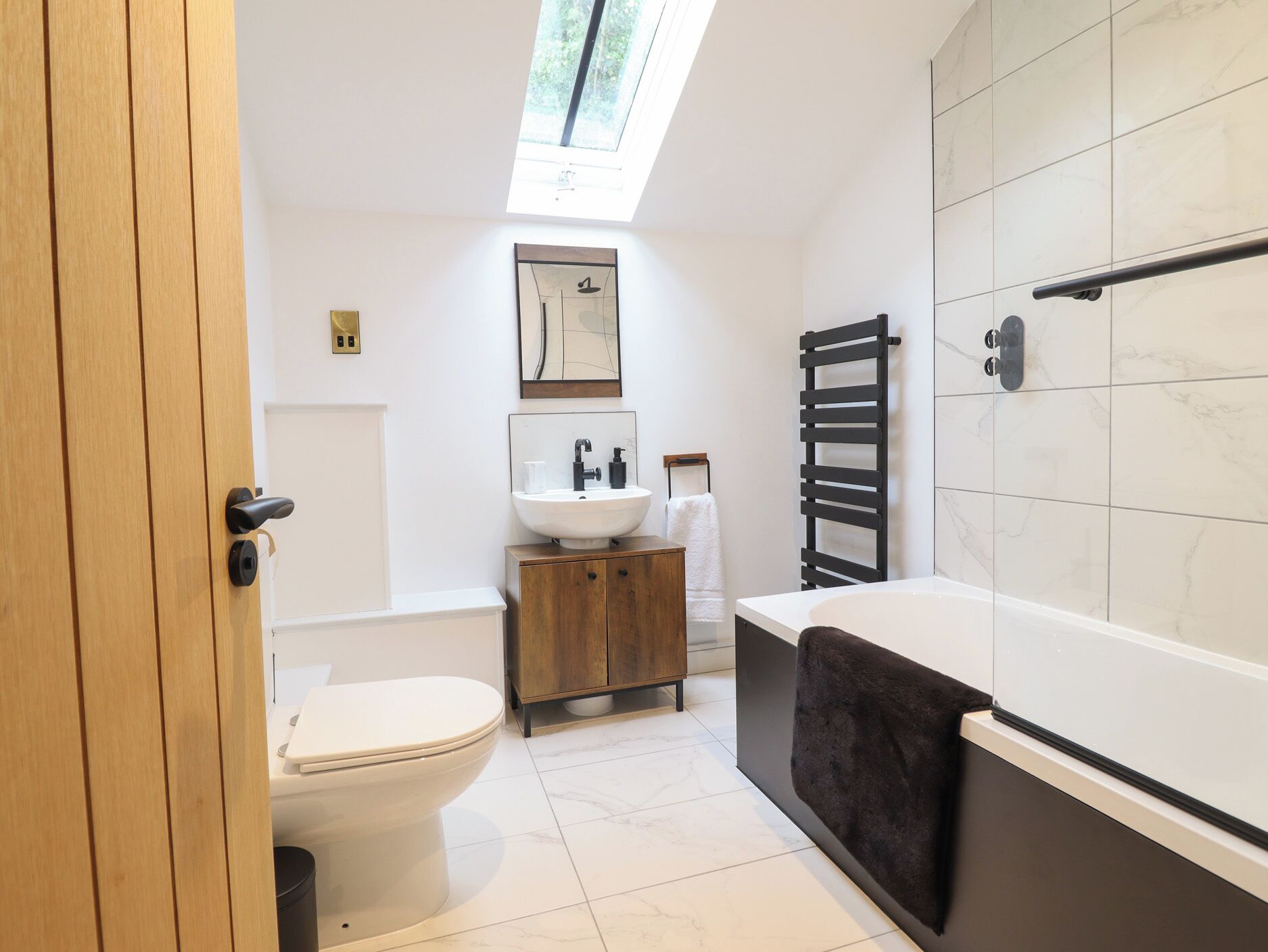 A modern bathroom with a skylight, a toilet, a sink, and a bathtub.