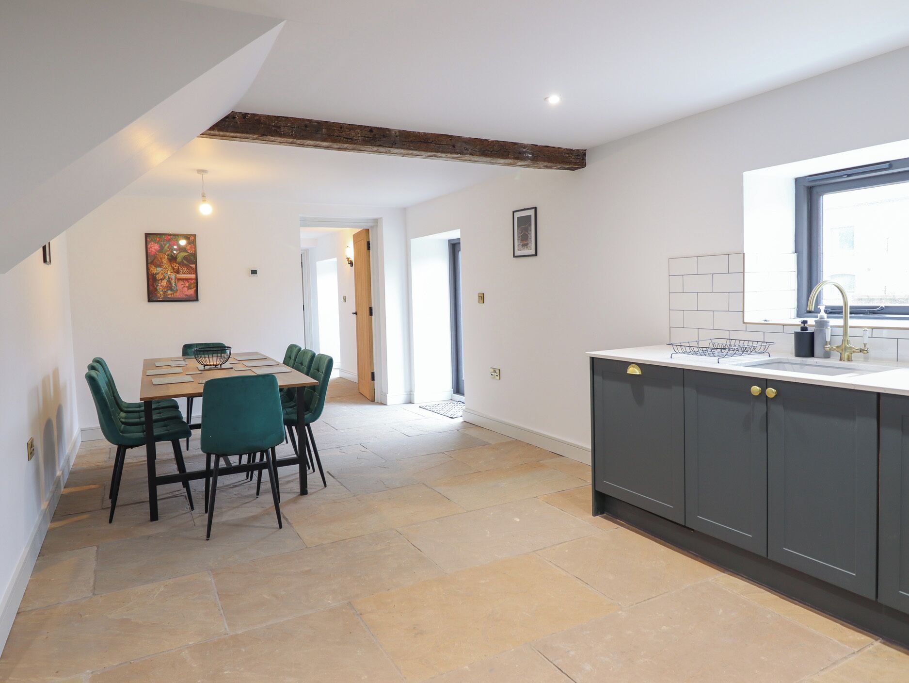 A modern kitchen with dark cabinets, a window, and a dining area with green chairs.