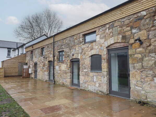 A stone building with multiple doors and windows, a wooden deck, and a paved walkway. - Sally's Barn (Oswestry)