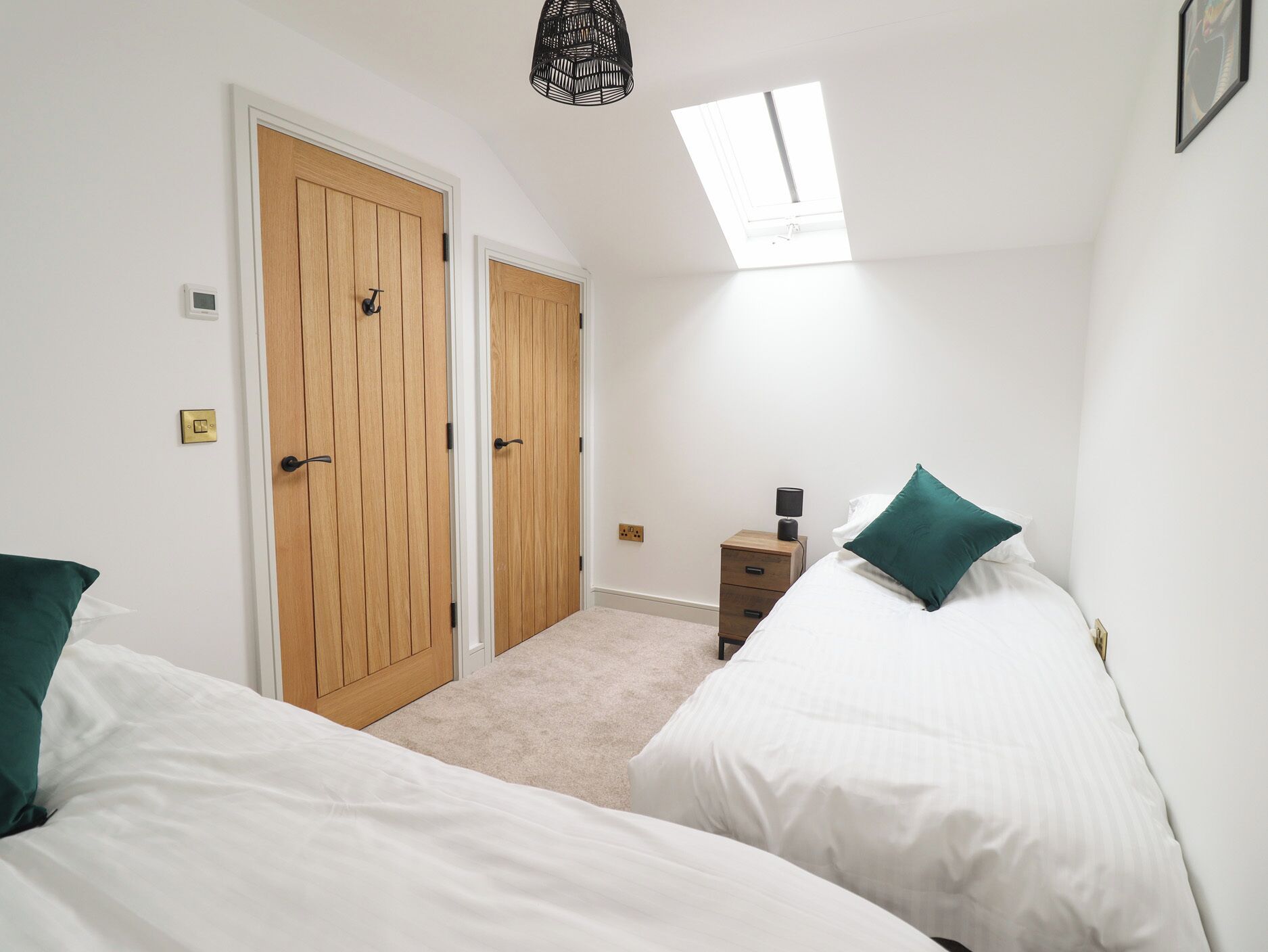 A bedroom with two beds, a skylight, wooden doors, a bedside table with a lamp, and a small nightstand.