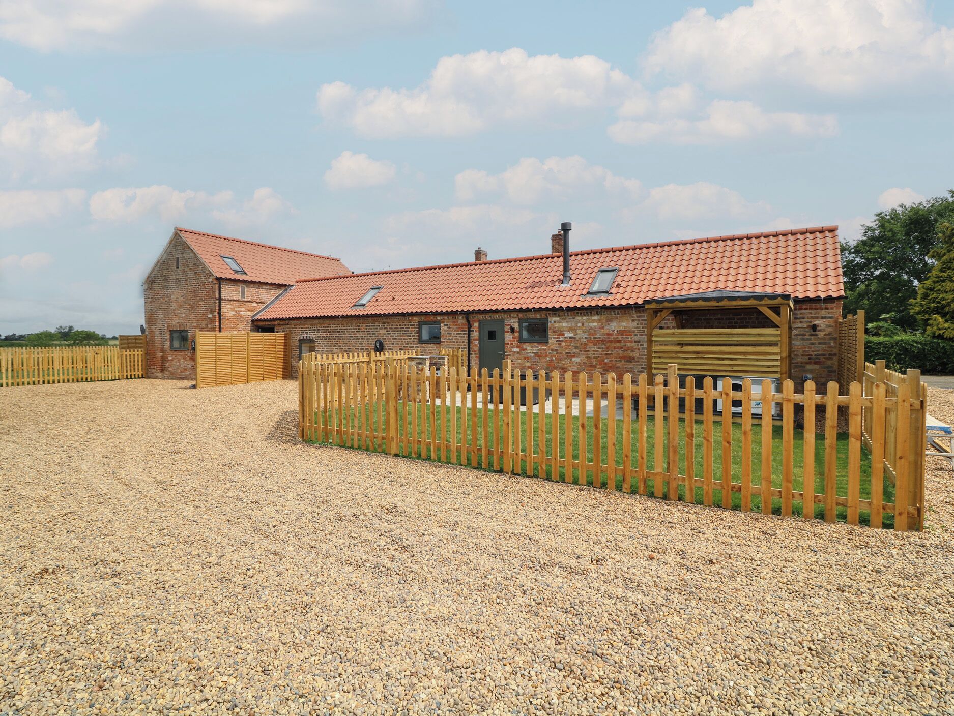 A brick barn with a red-tiled roof and a wooden fence.