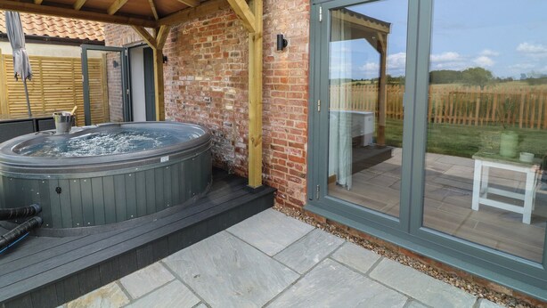 Un jacuzzi bajo una pérgola de madera junto a una puerta de vidrio que da a una terraza.