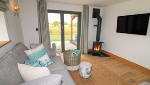 Una sala de estar con un sofá gris, una chimenea, un televisor montado en la pared y vistas al exterior.