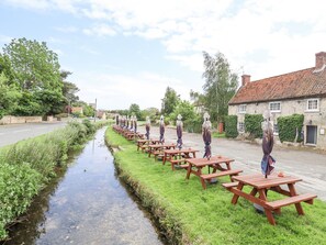 A row of picnic tables along a narrow water channel in a rural setting with stone buildings and greenery. - Buzzard Barn (Lincoln)