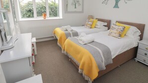 A bedroom with two beds, a desk, and a window with a view of greenery. - The Smithy (Chathill)