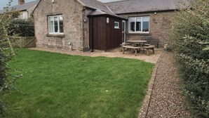 A stone house with a small backyard, a wooden table, and a shed. - The Smithy (Chathill)