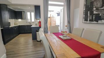 Uma cozinha moderna com armários escuros, uma mesa de jantar de madeira com um caminho vermelho e vista para a área de refeições através de uma porta de vidro.