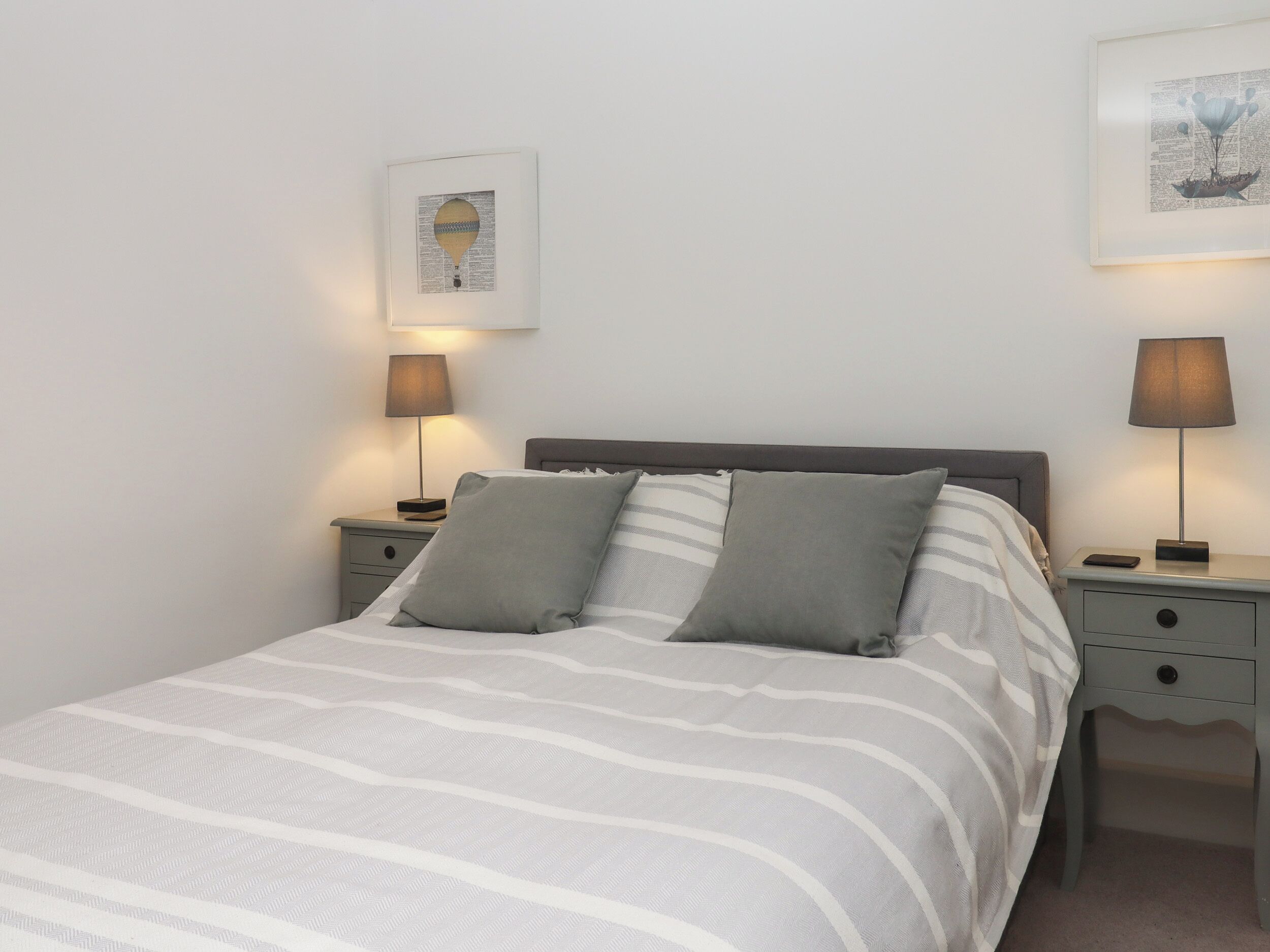 A neatly made bed with striped bedding, two bedside tables with lamps, and framed artwork on the walls.