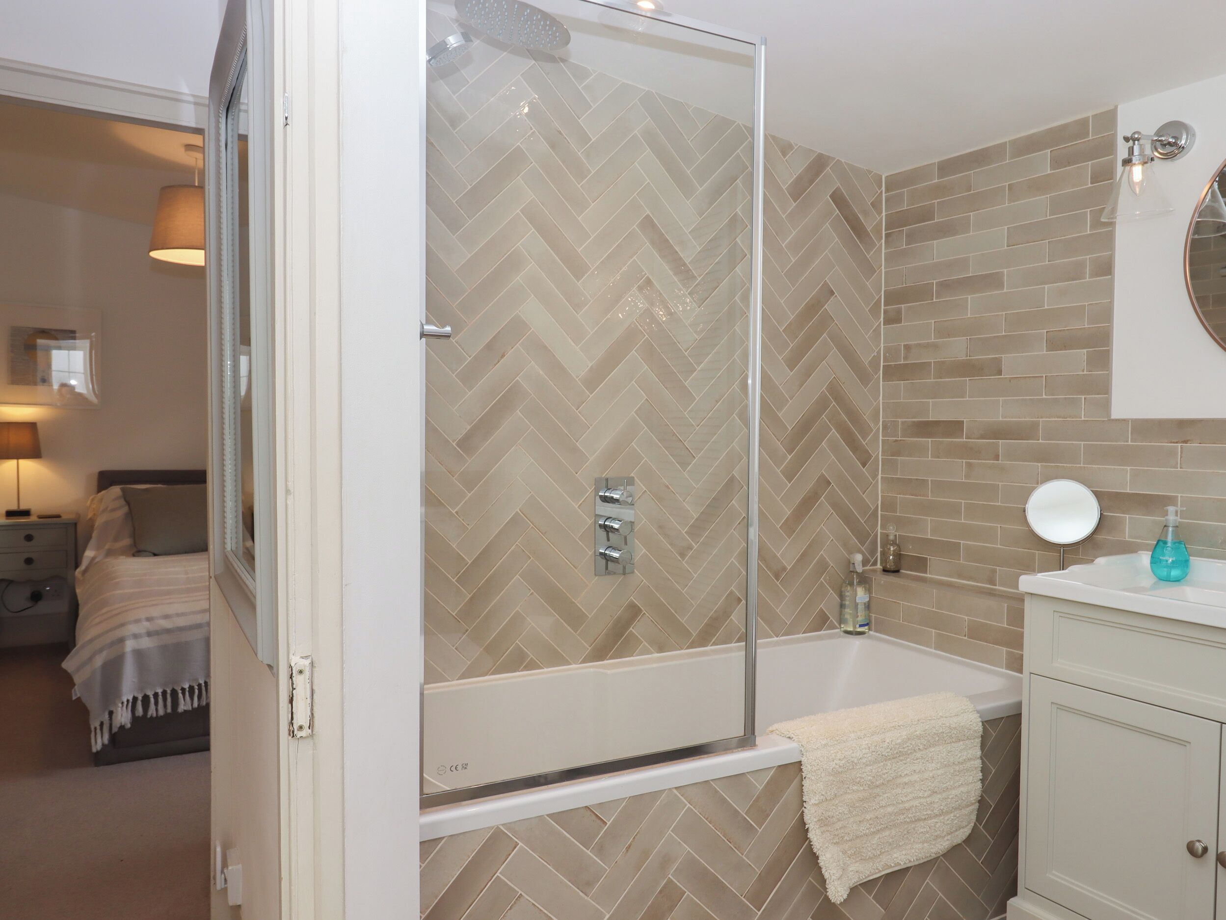 Un baño moderno con ducha envuelta en vidrio, una bañera blanca y un tocador con espejo y dispensador de jabón.