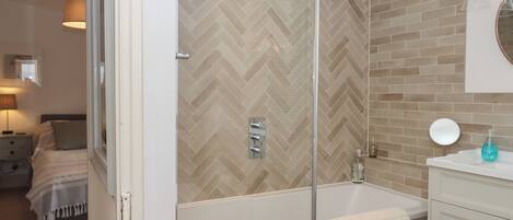 Un baño moderno con ducha envuelta en vidrio, una bañera blanca y un tocador con espejo y dispensador de jabón.