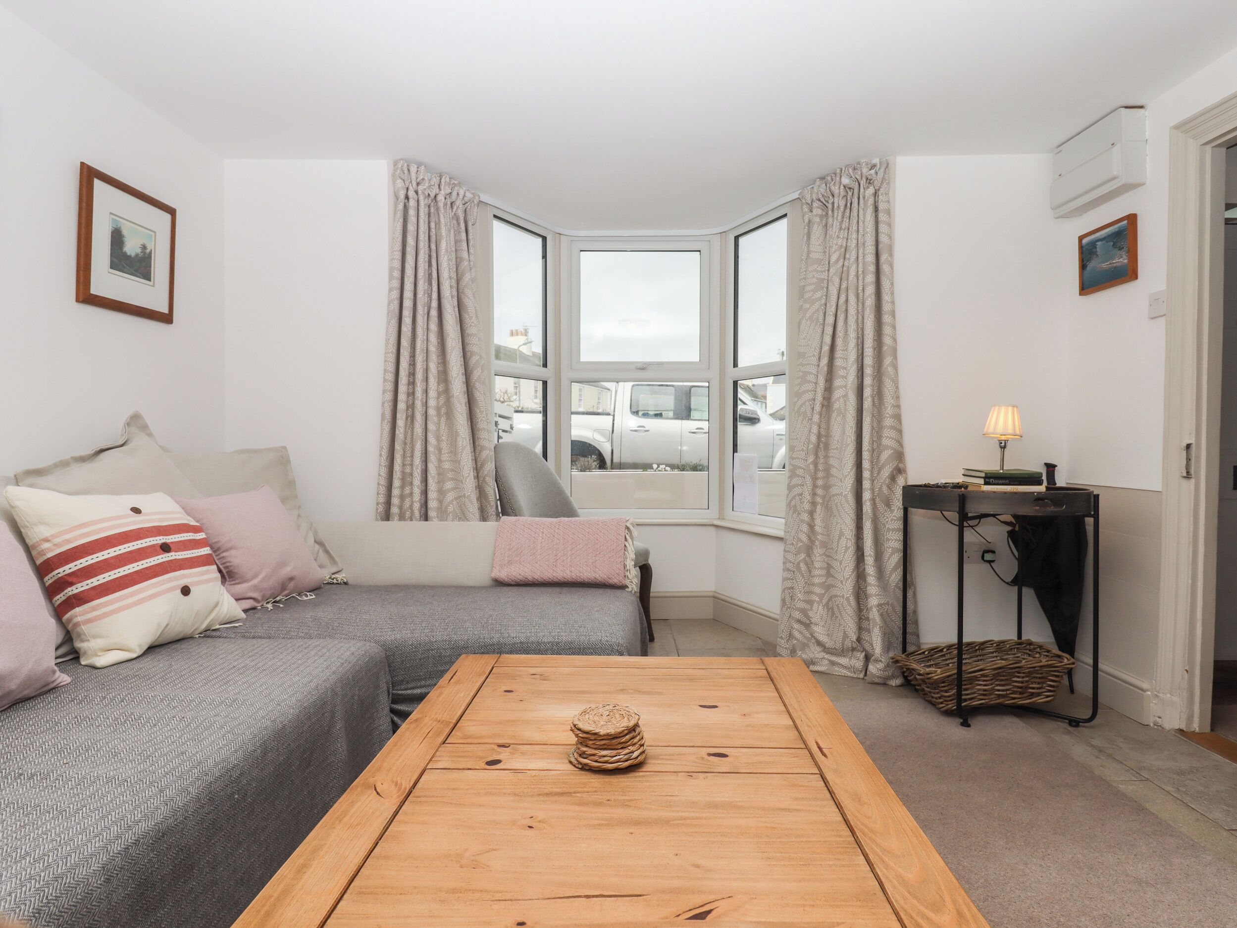A cozy living room with a grey sofa, a wooden coffee table, and a window with curtains.
