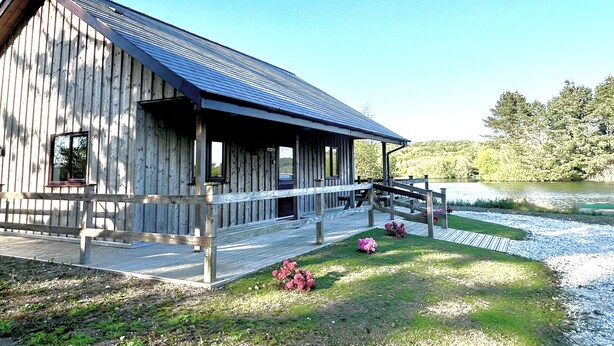 A wooden cabin with a porch and a small deck by a lake. - Kingfisher Lodge (St Austell)
