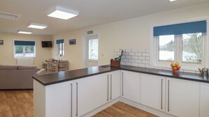 A modern kitchen with white cabinets, a black countertop, and a window with a view of trees. - Kingfisher Lodge (St Austell)