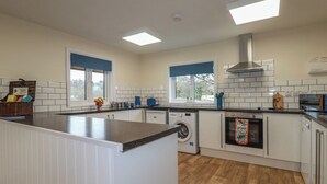 A modern kitchen with a central island, built-in appliances, and large windows. - Kingfisher Lodge (St Austell)