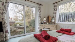 Ein Schlafzimmer mit Bett, Kommode, Spiegel und Blick ins Freie.