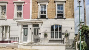 A row of townhouses with white and pink facades, numbered doors, and a small front garden with a metal fence. - Flat 4 - Hengistbury (Bournemouth)