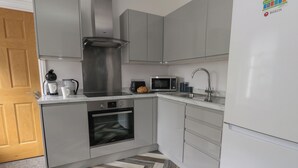 A modern kitchen with grey cabinets, a stainless steel range hood, a built-in oven, a microwave, and a sink. - Flat 4 - Hengistbury (Bournemouth)