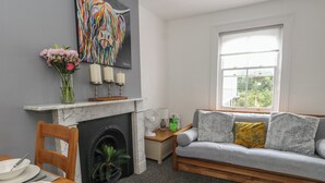 A living room with a fireplace, a sofa, a dining table with plates, and a painting on the wall. - Flat 4 - Hengistbury (Bournemouth)