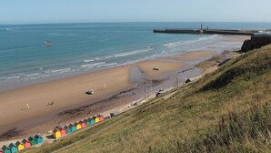 A coastal beach with a pier, beach huts, and a lighthouse. - Juniper Lodge (Whitby)