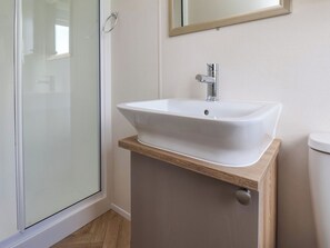 A bathroom with a white sink, a mirror above it, and a glass shower door. - Juniper Lodge (Whitby)