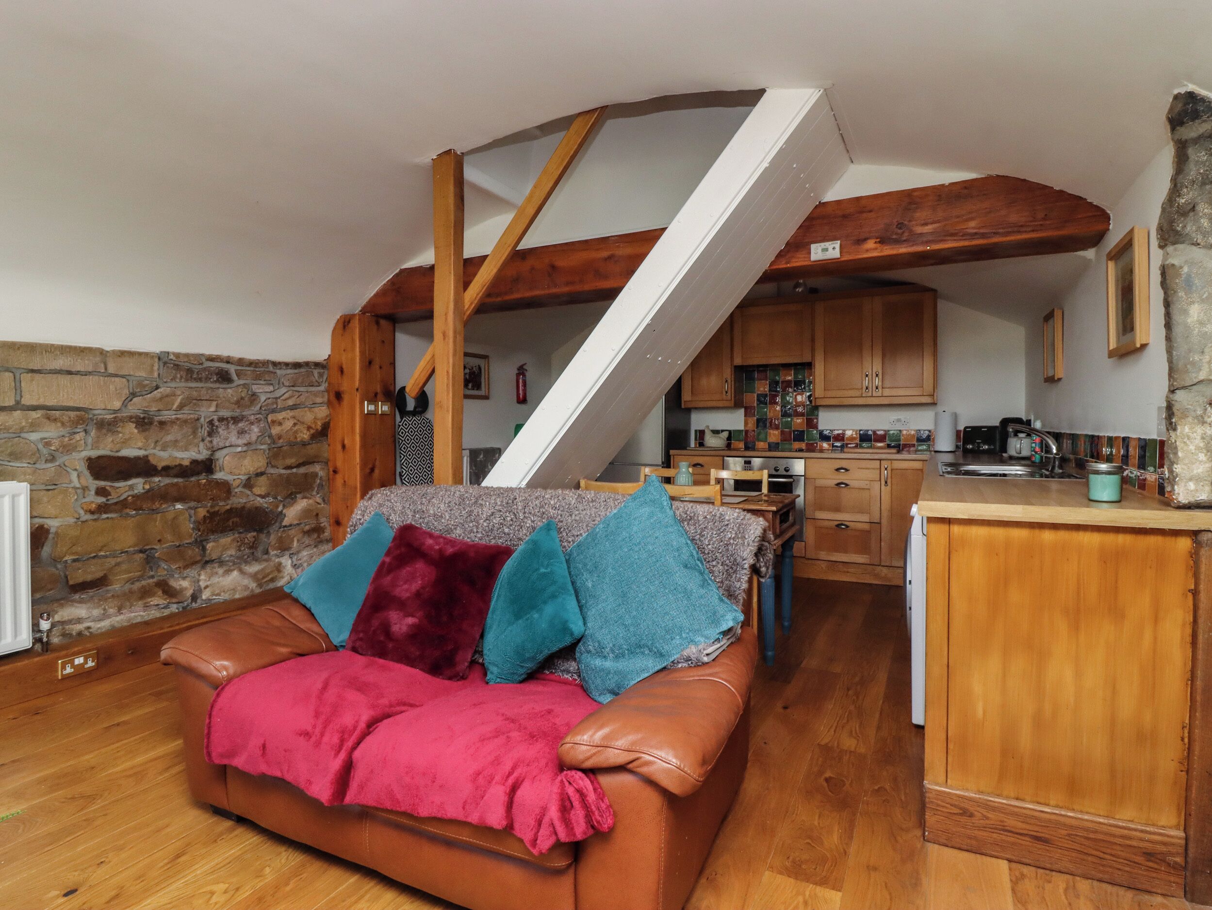 Un loft acogedor con una escalera de madera, una cocina con armarios de madera y un sofá de cuero con cojines de colores.