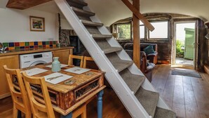 Eine rustikale Küche mit Holzbalken, einem Esstisch mit Stühlen, einer Treppe und Blick ins Freie.