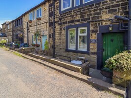 Una hilera de casas de piedra con una puerta verde, un letrero que dice "Pike View Cottage", y un pequeño jardín con plantas en macetas.