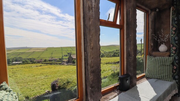 Ein rustikaler Raum mit einem großen Fenster, das einen Blick auf eine grüne Landschaft und ein entferntes Dorf bietet.