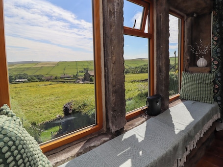 A rustic room with a large window offering a view of a green landscape and a distant village.