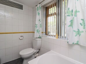 Een badkamer met een toilet, een bad en een raam met gordijn.