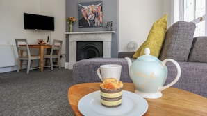 A cozy living room with a fireplace, a television mounted on the wall, a dining area with a table and chairs, and a sofa with cushions. - Flat 3 - Muderford (Bournemouth)