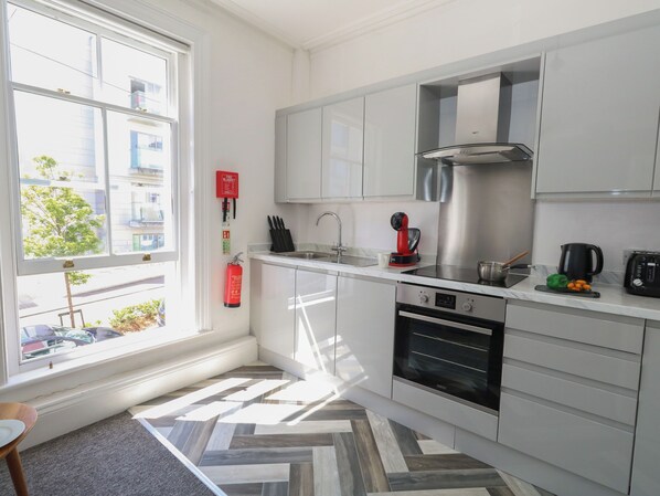 A modern kitchen with white cabinets, stainless steel appliances, and a herringbone-patterned floor. - Flat 3 - Muderford (Bournemouth)