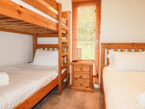 A room with two wooden bunk beds, a small wooden nightstand with a lamp, and a window with blinds. - 1 Hedgerows (Looe)