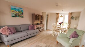 Un salon avec un canapé gris, un fauteuil vert, un meuble en bois et un coin repas comprenant une table et des chaises.