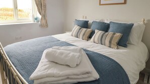 Un lit bien fait, recouvert d’une couvre-lit bleue et blanche, avec deux oreillers et une serviette blanche pliée posée sur le lit.