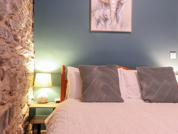 Une chambre avec un mur en pierre, un lit avec deux oreillers, une table de chevet avec une lampe et un tableau accroché au mur.