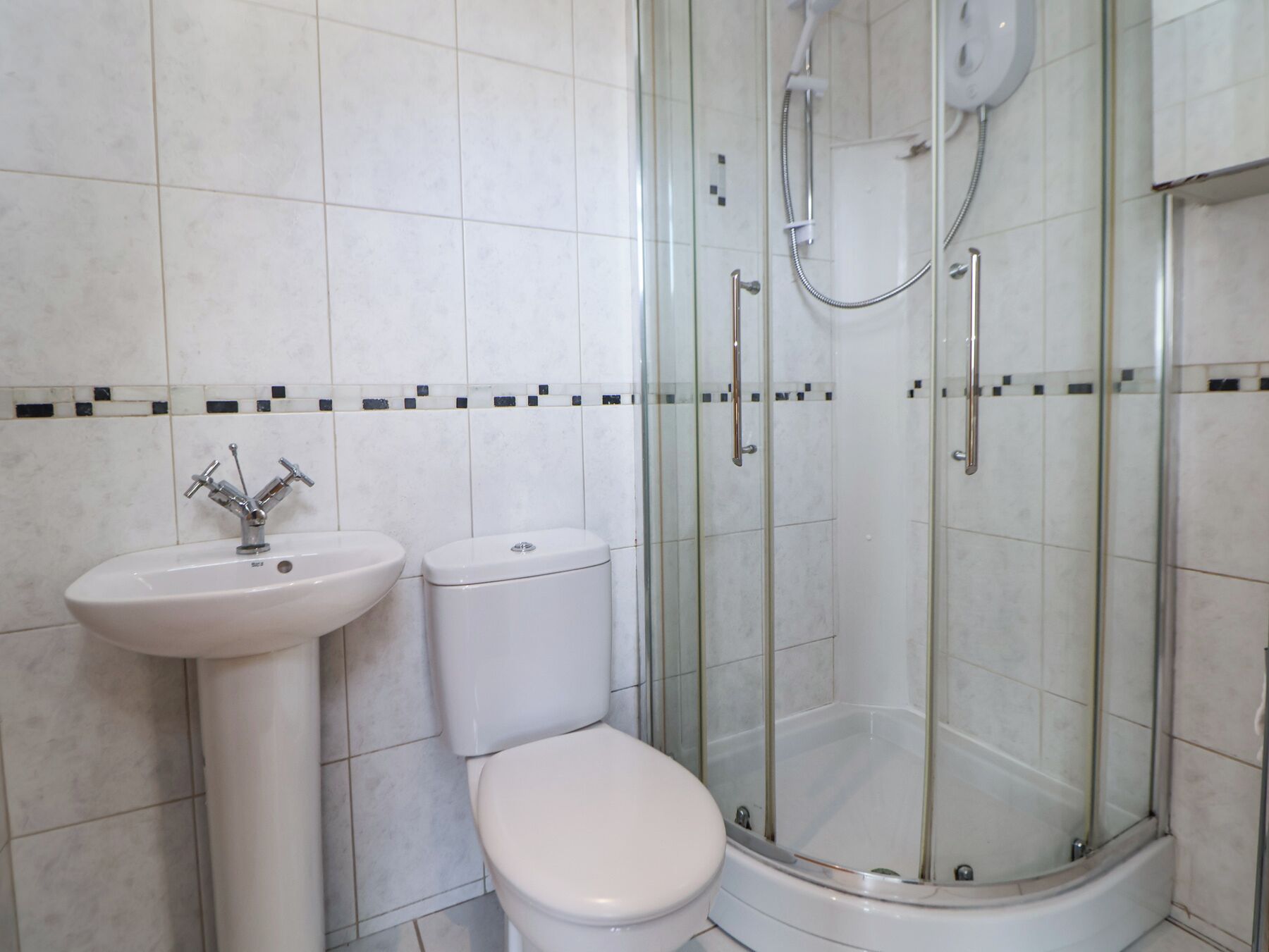 Un baño con ducha de vidrio, lavamanos pedestal y retrete.