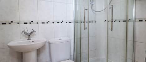 Un baño con ducha de vidrio, lavamanos pedestal y retrete.